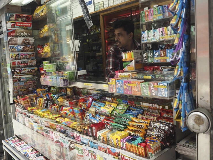 an asian vendor stands behind the counter full of snacks