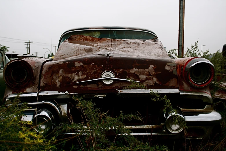 an old and rusty classic car in weeds