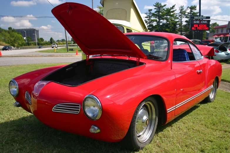 an old red sports car with a hatch open at a show