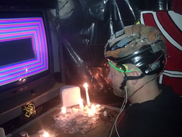 a man with a helmet standing in front of a tv holding a lit candle