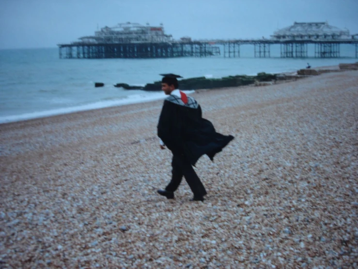 a man in a graduation cap and robe walks along a beach