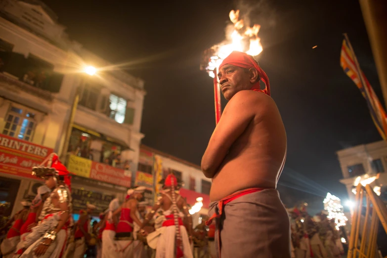 an old man in a headdress stands with torches