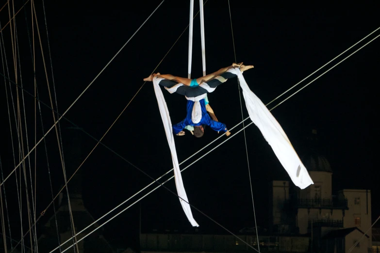 two people high above the ground as one attempts to hang on a tightrope