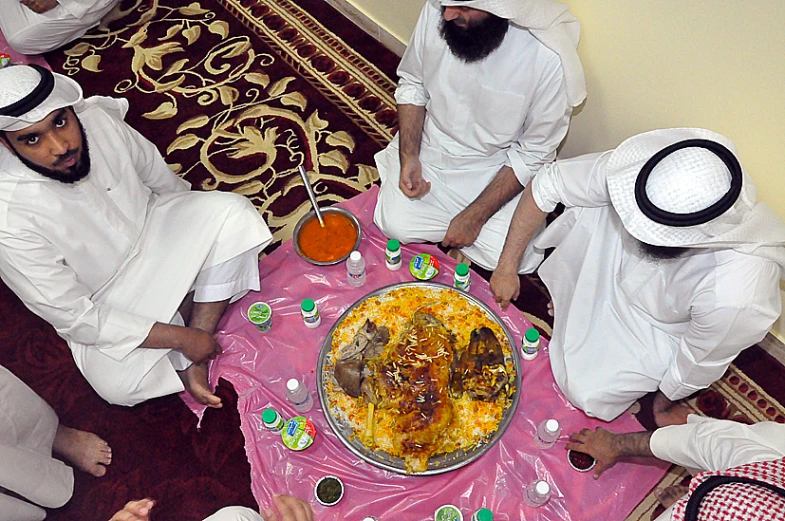 a group of people dressed in white and sitting at a table with a meal on it