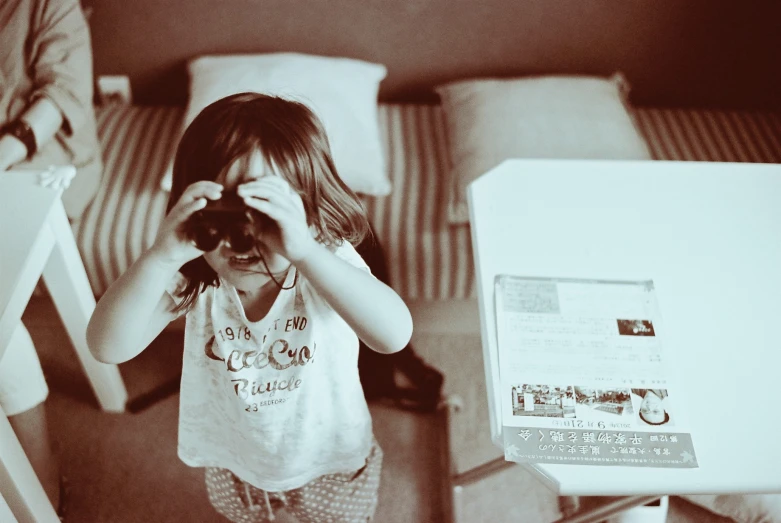 a little girl covering her face and looking through a binoculars