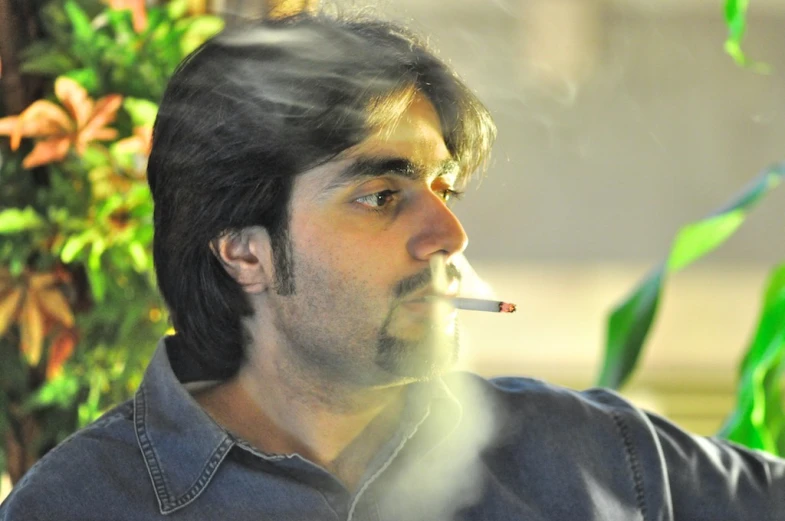 a man smoking a cigarette in front of plants