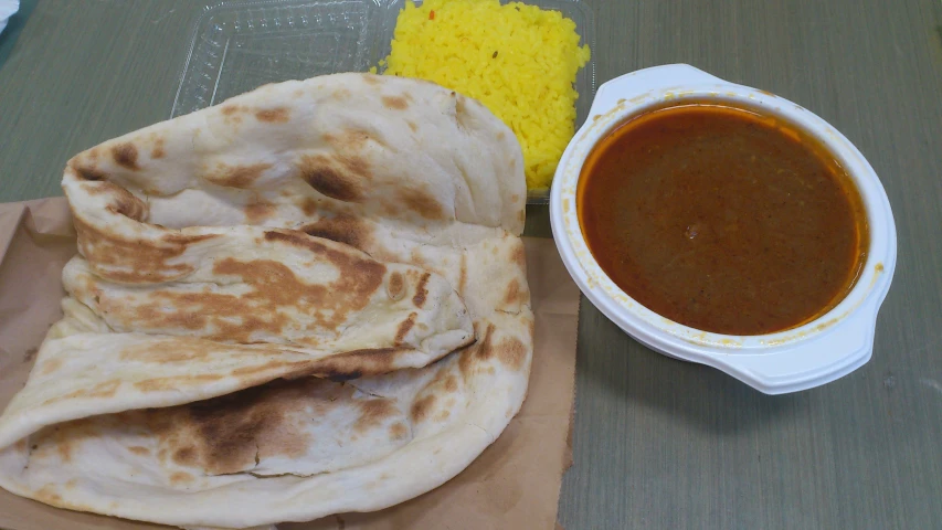 a plate with pita bread, bowl of sauce and yellow rice