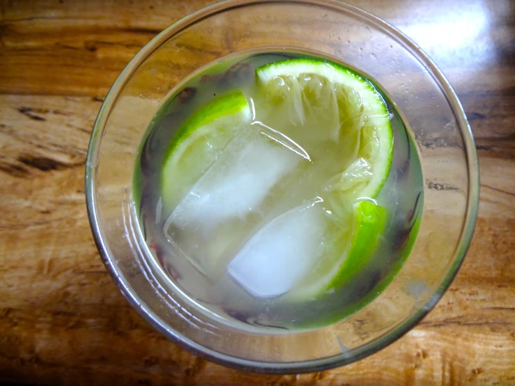 a clear bowl with some green lemons and an ice on it