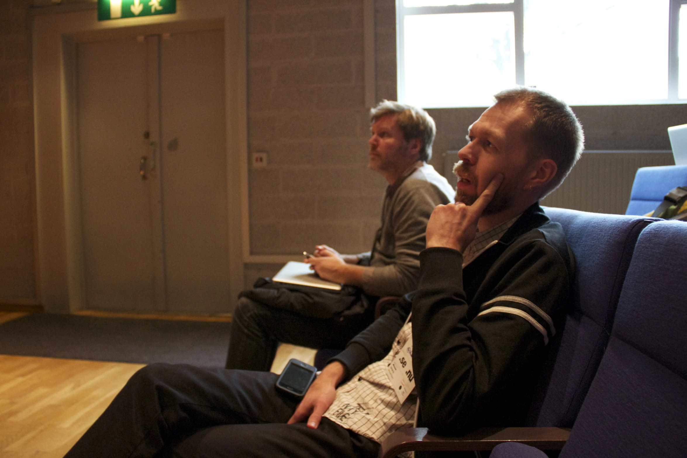 two men are sitting together, one is looking to his left