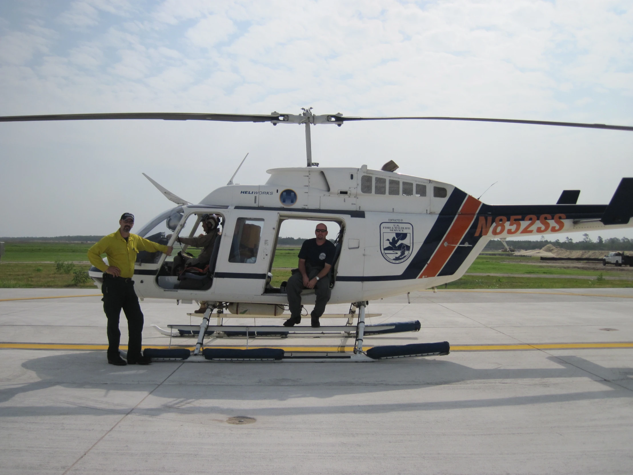 two men in black and yellow stand at the front of a helicopter