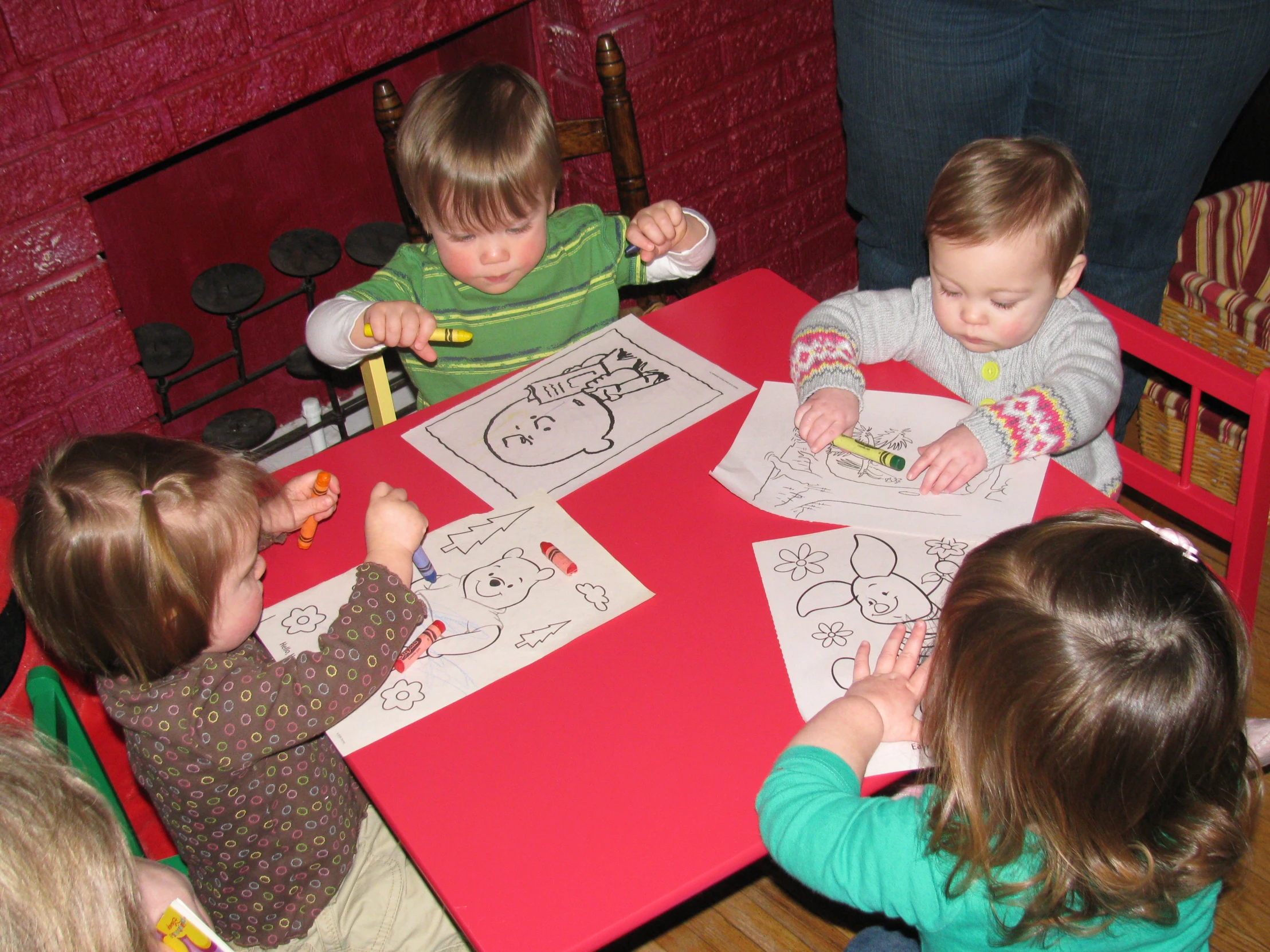 five little children with color pencils sitting at a red table