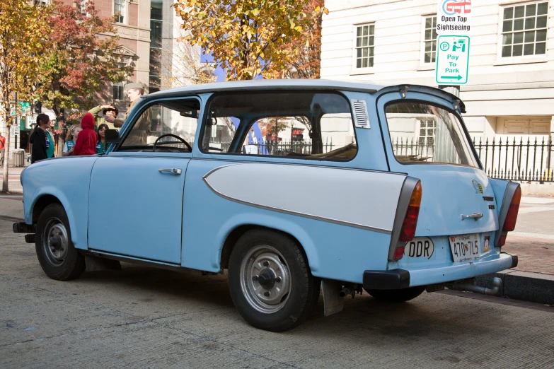 an old car sitting in a street with pedestrians