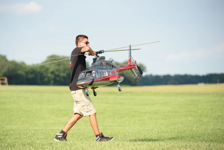 the man is walking through the green field with his helicopter