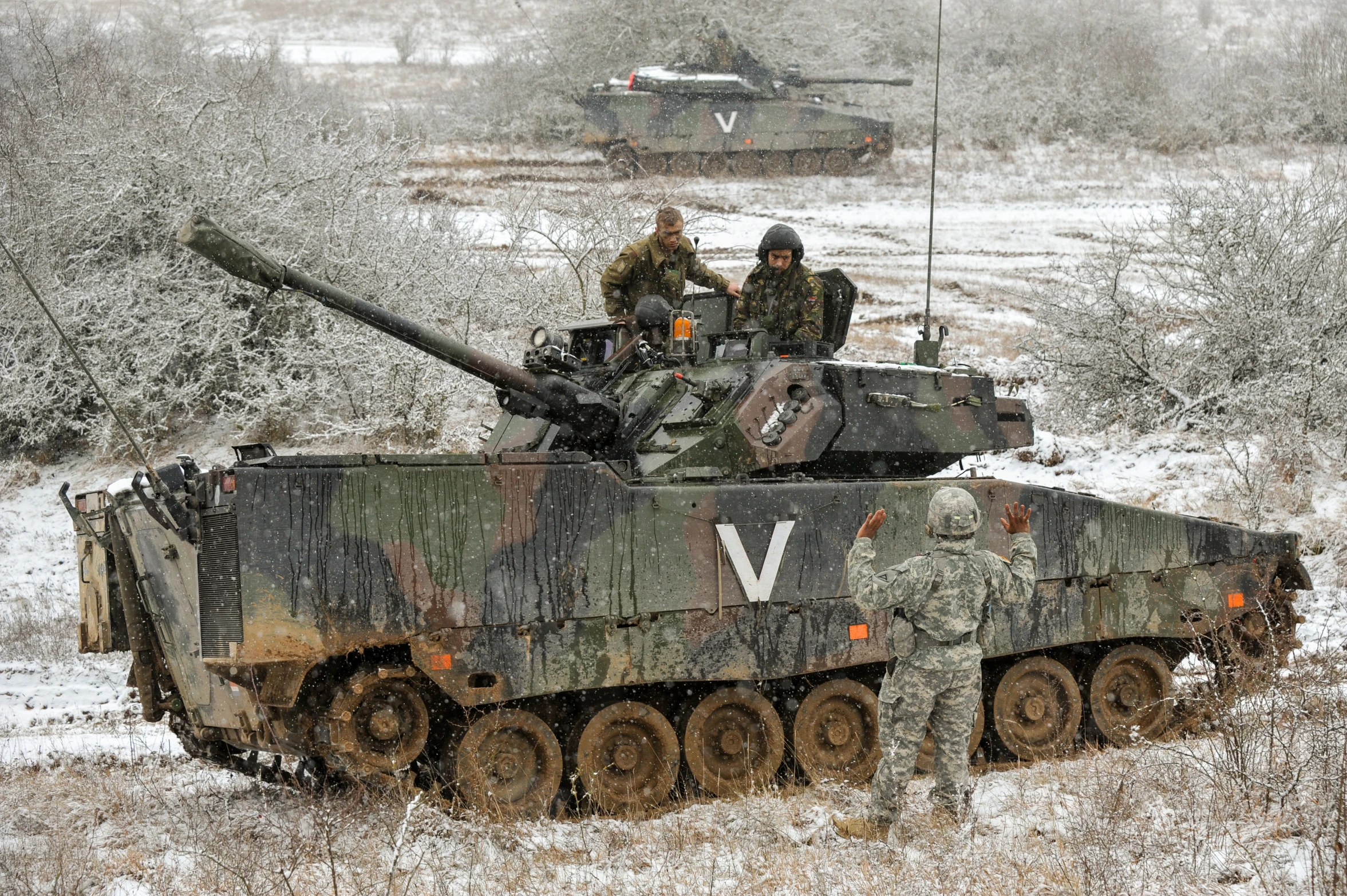 tanks with soldiers driving in the snow near an army base