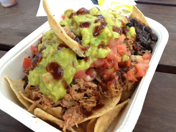 a bowl filled with nachos and toppings sitting on top of a wooden table