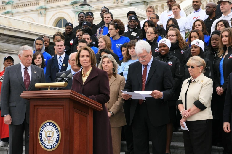 several people stand in front of a large building while a speaker holds up paper