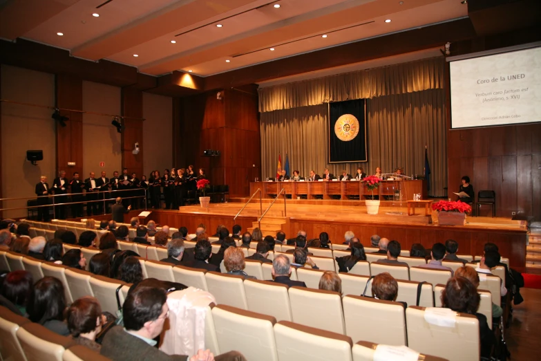 large room with rows of seats and people standing in front of the podium