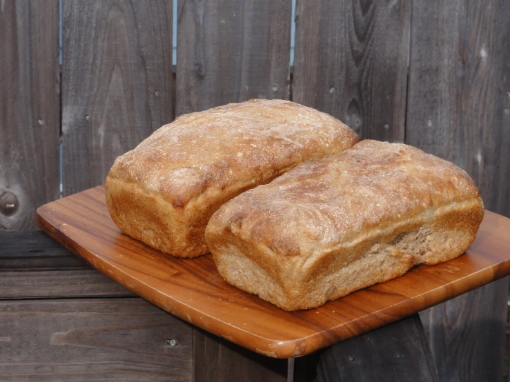 two large loaves of bread sit on a wooden  board