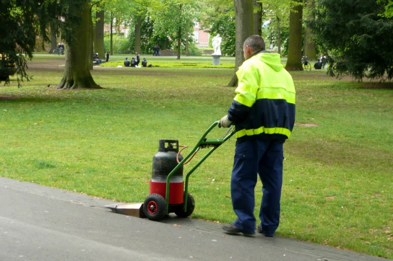 a person hing a lawn mower on a paved path in the park