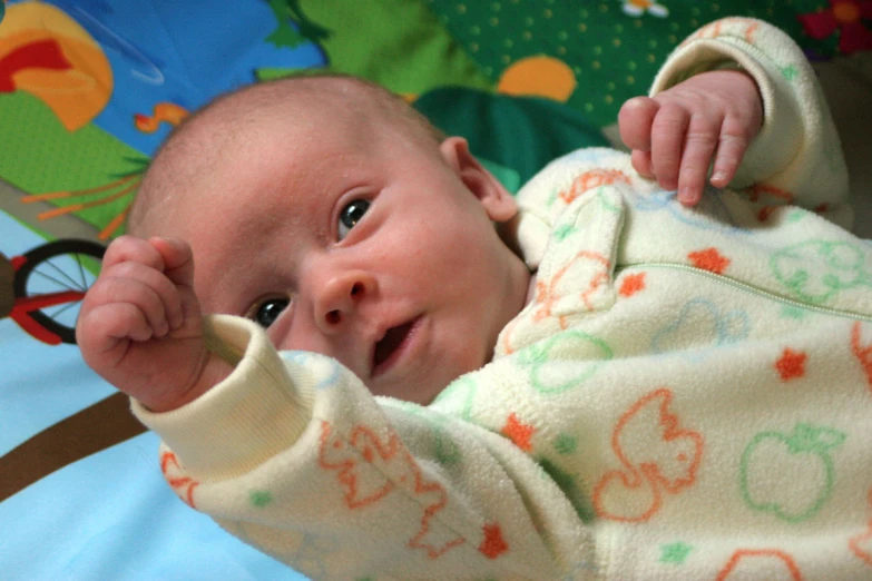 a baby sitting on top of a bed holding his hand in the air