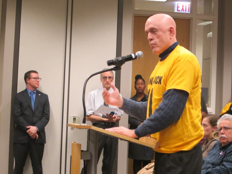 a man is speaking at an event with people watching