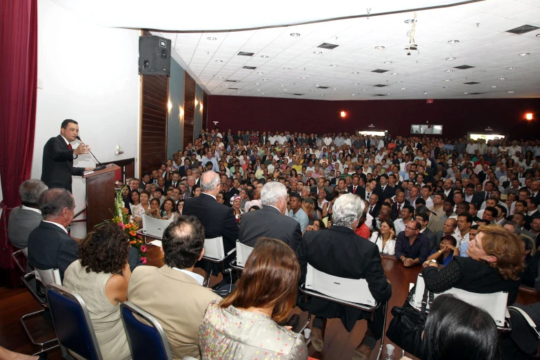 a crowd is sitting and one person stands at the microphone