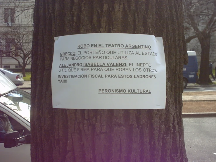 a sign taped to a tree in front of some cars