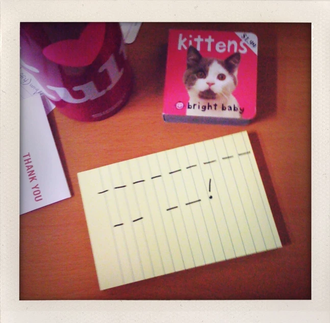 a note pad on a desk, a cup and a kittens book