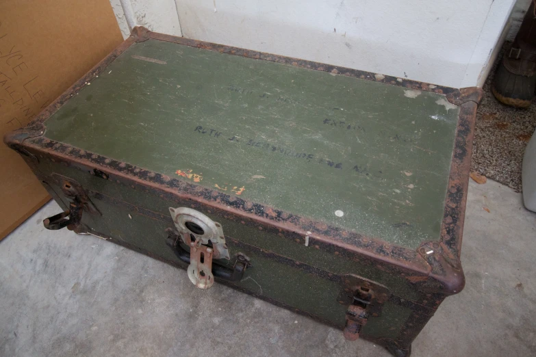 an old, vintage green suitcase sits next to a cardboard box