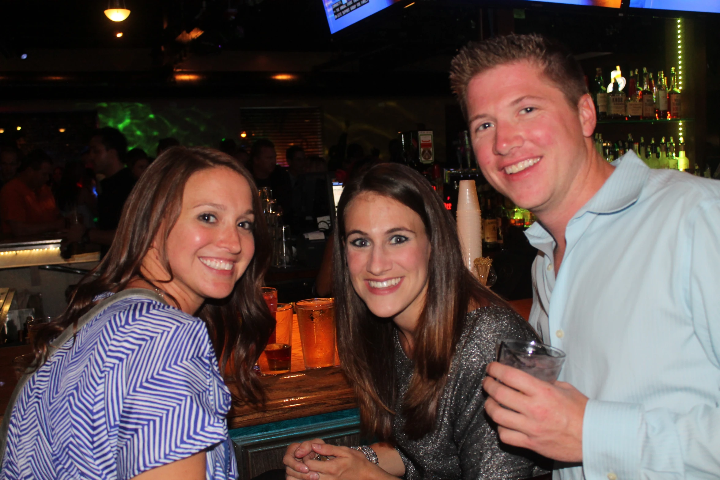 three friends smile while holding drinks in a bar