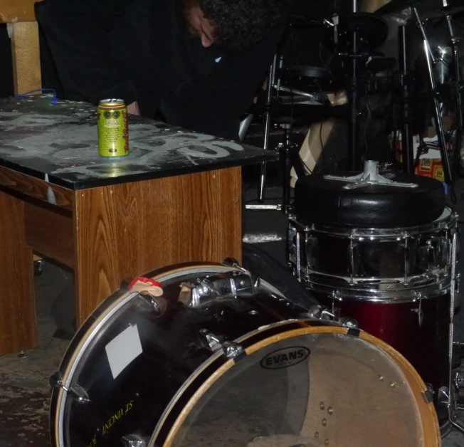 a man with a beard playing drums and holding a drink