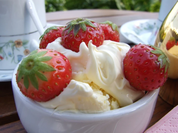 a bowl with strawberries, whipped cream and spoons on it