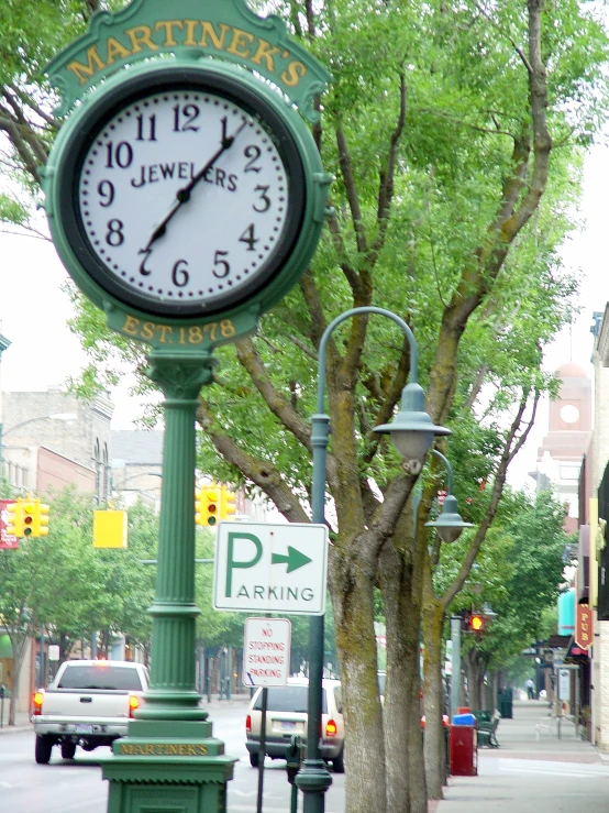 a clock on a post near street signs and trees