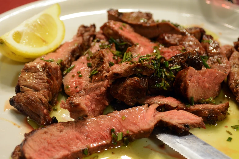 a white plate with meat and a knife on it