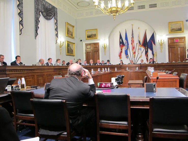 men in suits are sitting around a large conference room