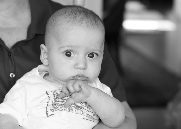 a baby is in a white shirt while holding it's owner