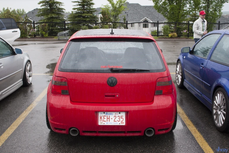 two cars parked in front of a fence and some people in the background