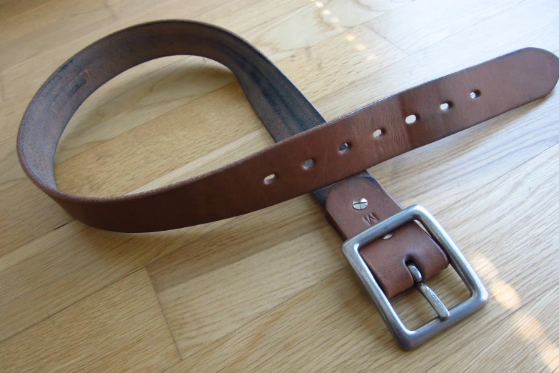 a wooden floor has a brown belt and a buckle on it
