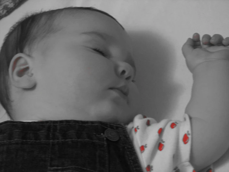 a black and white image of a young baby sleeping on the bed