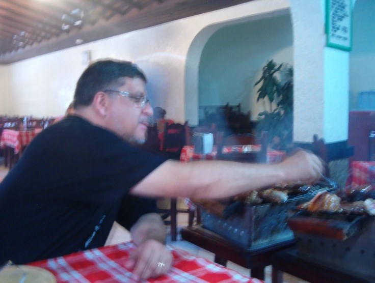 man in glasses sitting at a red checkered table with food on it