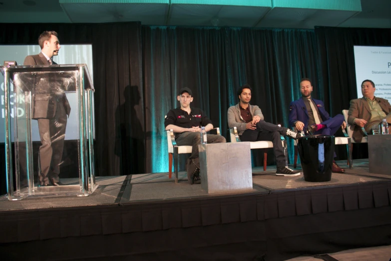 five people sitting in chairs while a speaker stands