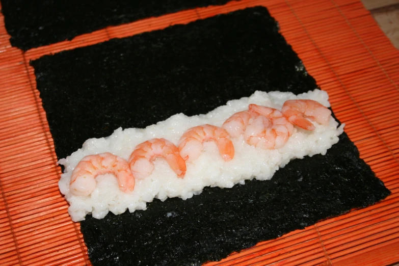 a rectangular sushi with shrimp and cauliflower on a wooden mat