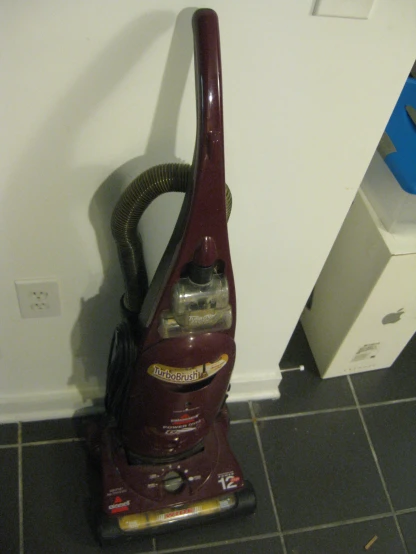 a red and black vacuum on tile next to wall