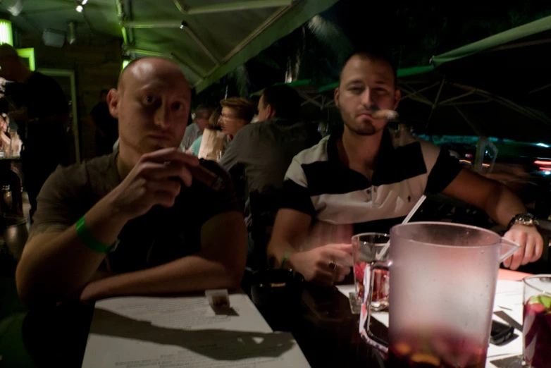 two men sitting at a table looking at their cell phones