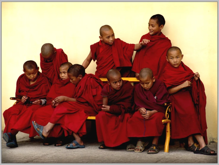 nine monks in red robes sitting and standing with their legs crossed on a chair