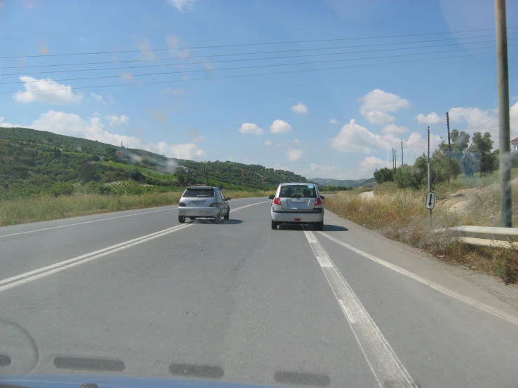 two cars driving down an empty highway next to hill side