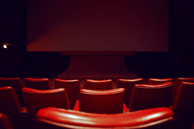 an empty theater with red seats and a large screen