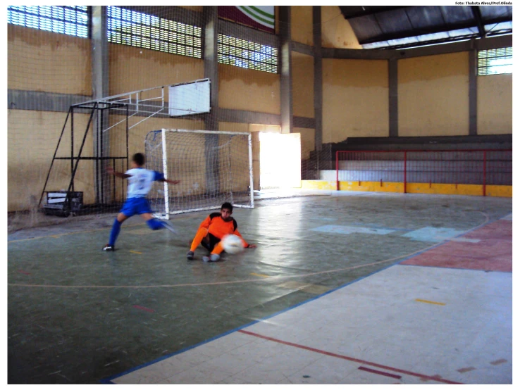 two boys playing soccer inside a gym