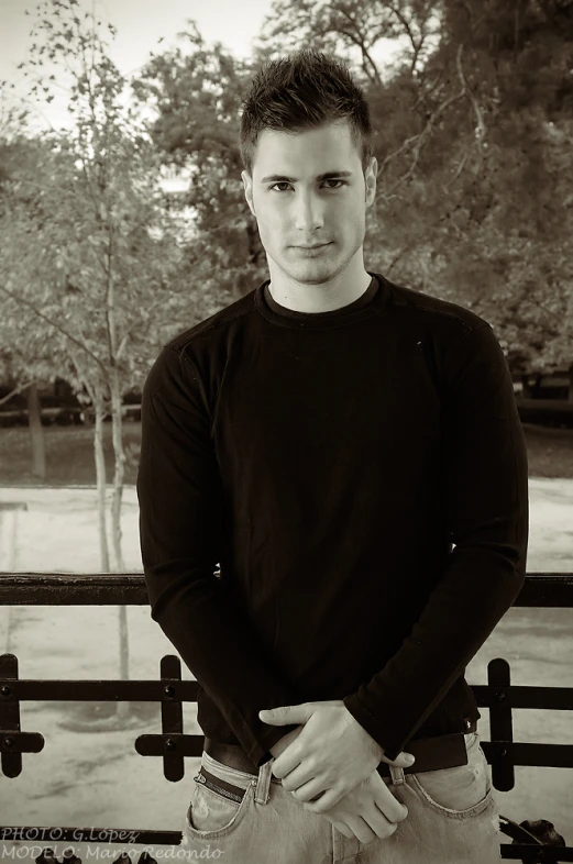 a man leaning against a fence while wearing a sweater