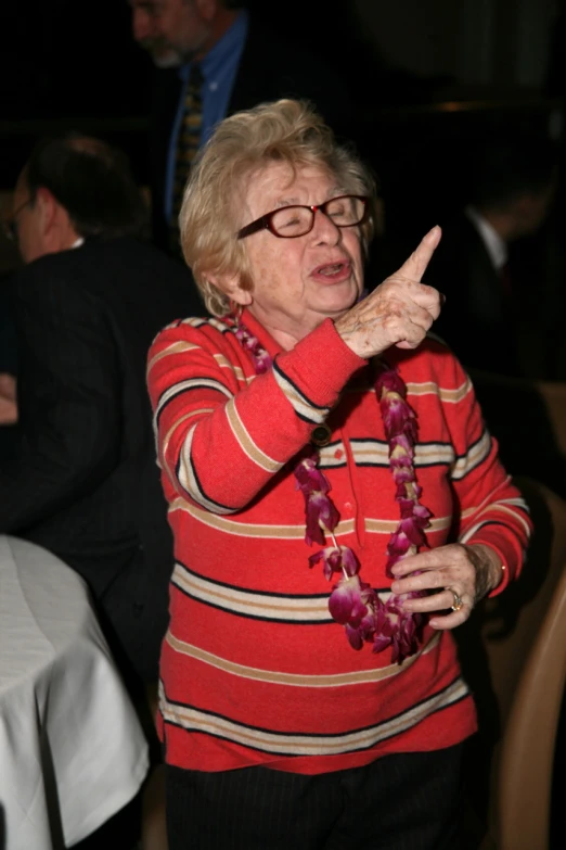 a woman wearing glasses and a floral necklace holding her index up